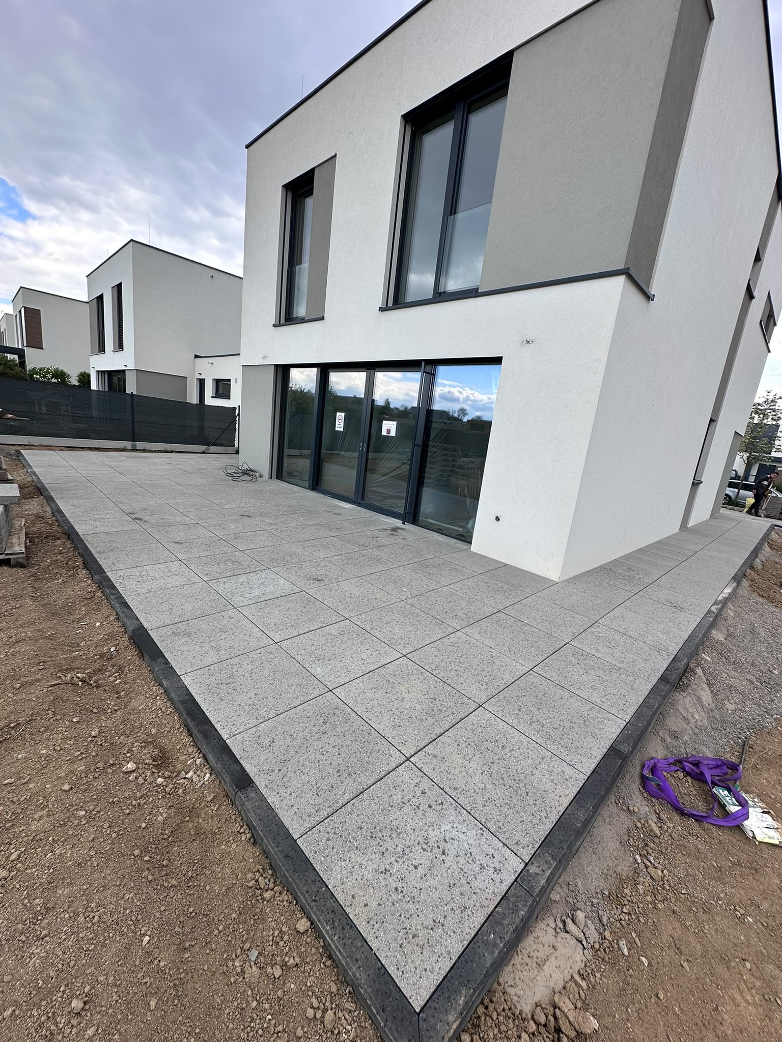 Terasa z velkoformátových betonových dlaždic s tmavým obrubníkem u moderního domu