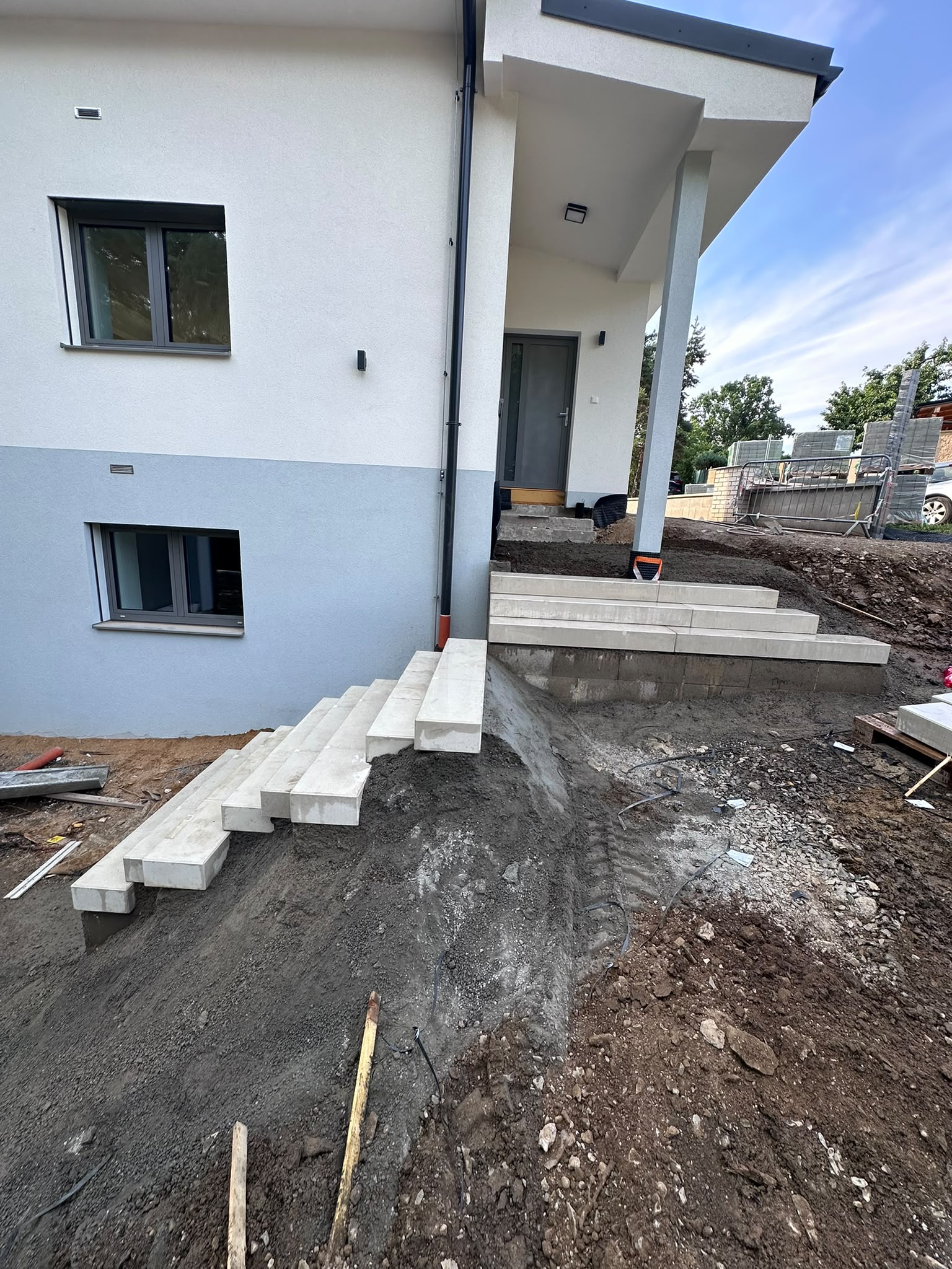 Výkopy a terénní úpravy u vstupu do domu s rozestavěným betonovým schodištěm